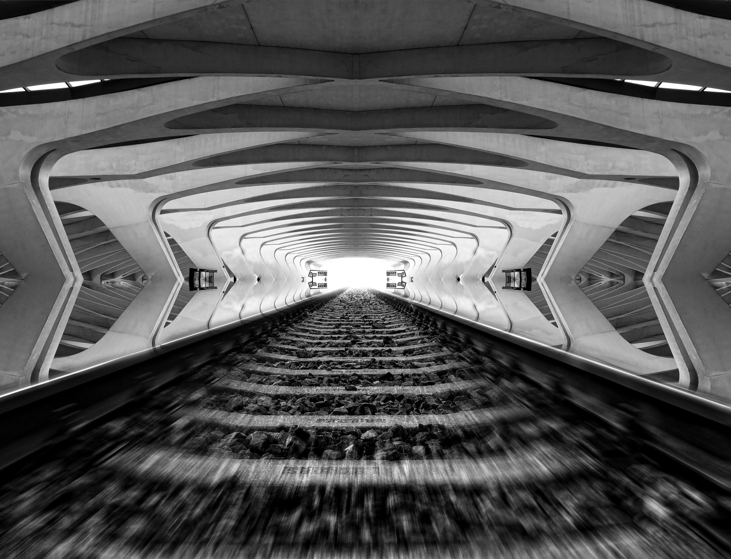 Railway track receding through a symmetrical concrete tunnel toward bright daylight